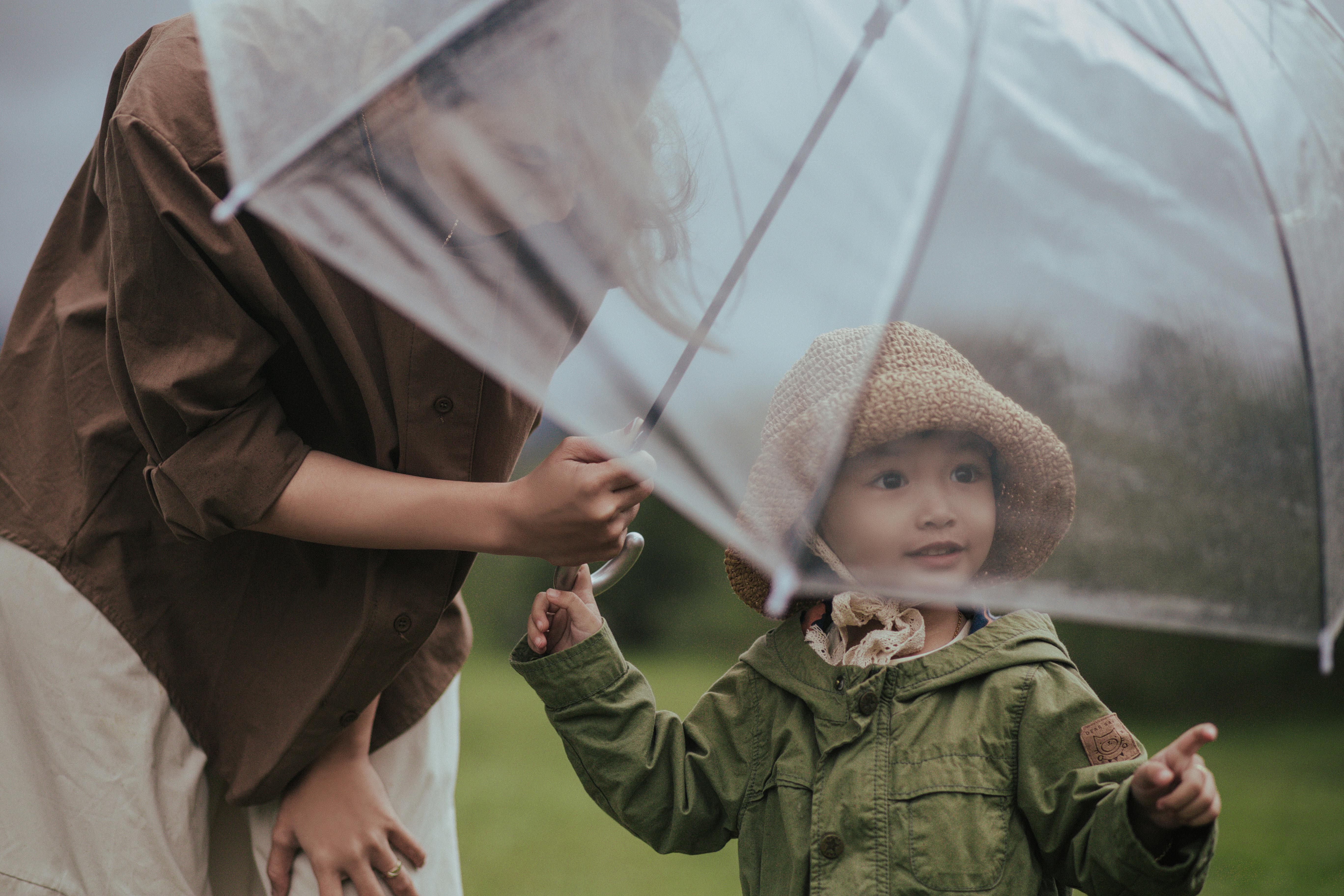 Parent and child sharing a clear umbrella in the rain